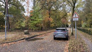 Blick in den Fuchssteinerweg in Berlin Reinickendorf mit herbstlichen Bäumen, einem am Straßenrand abgestellten grauen Auto und einem Straßenschädenschild.