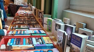 Lange Reihen roter und gelber Kisten voller Bücher auf Tischen in einem Saal, an der Fensterbank stehen weitere Bücher aufgestellt.