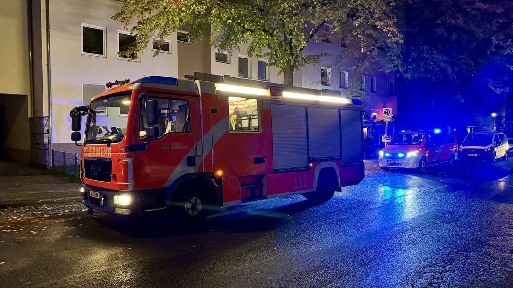 Löschfahrzeug der Berliner Feuerwehr und Rettungswagen mit Blaulicht vor einem Mehrfamilienhaus am Abend