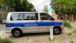 Silberner Kleinbus mit blauem Streifen und der Aufschrift „Bezirksamt Reinickendorf von Berlin, Ordnungsamt“ auf Kopfsteinpflaster vor Altbauten