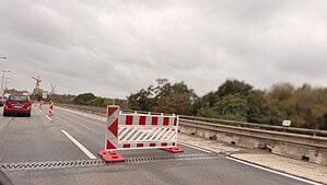 Rot-weiße Absperrung auf dem rechten Fahrstreifen einer Autobahnbrücke, links fließt der Verkehr weiter.