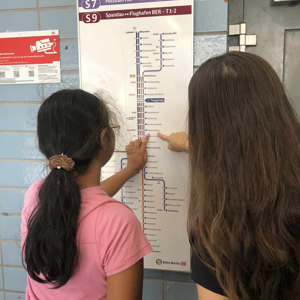 Ein Mädchen in rosa T-Shirt und eine junge Frau mit langen braunen Haaren stehen mit dem Rücken zur Kamera vor einem S-Bahn-Linienplan und zeigen mit dem Finger auf Stationen.