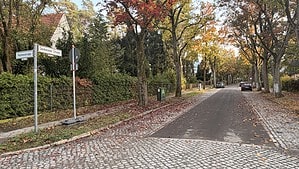 Blick von der Ecke Huttenstraße in die Senheimer Straße in Frohnau mit asphaltierter Fahrbahn, gepflasterten Randstreifen, Straßenschildern und herbstlich gefärbten Bäumen