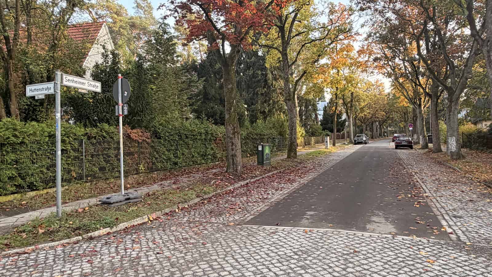 Blick von der Ecke Huttenstraße in die Senheimer Straße in Frohnau mit asphaltierter Fahrbahn, gepflasterten Randstreifen, Straßenschildern und herbstlich gefärbten Bäumen