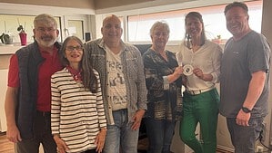 Sechs Personen stehen in einem Büroraum, zwei Frauen in der Mitte halten gemeinsam eine runde Plakette mit dem Bezirkswappen