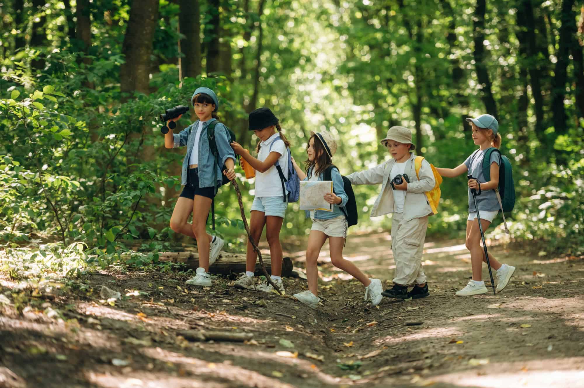 Fünf Kinder mit Rucksäcken wandern durch einen Wald.