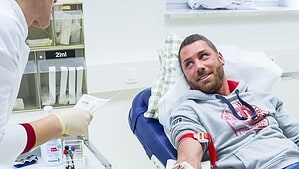 Ein Mann liegt in einem medizinischen Stuhl und spendet Blut, während medizinisches Personal im Behandlungsraum steht.
