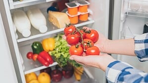Eine Person legt rote Tomaten in einen gut gefüllten Kühlschrank.