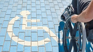 Ein Mensch im Rollstuhl fährt über blau gefärbtes Pflaster mit aufgemaltem weißem Rollstuhlsymbol.